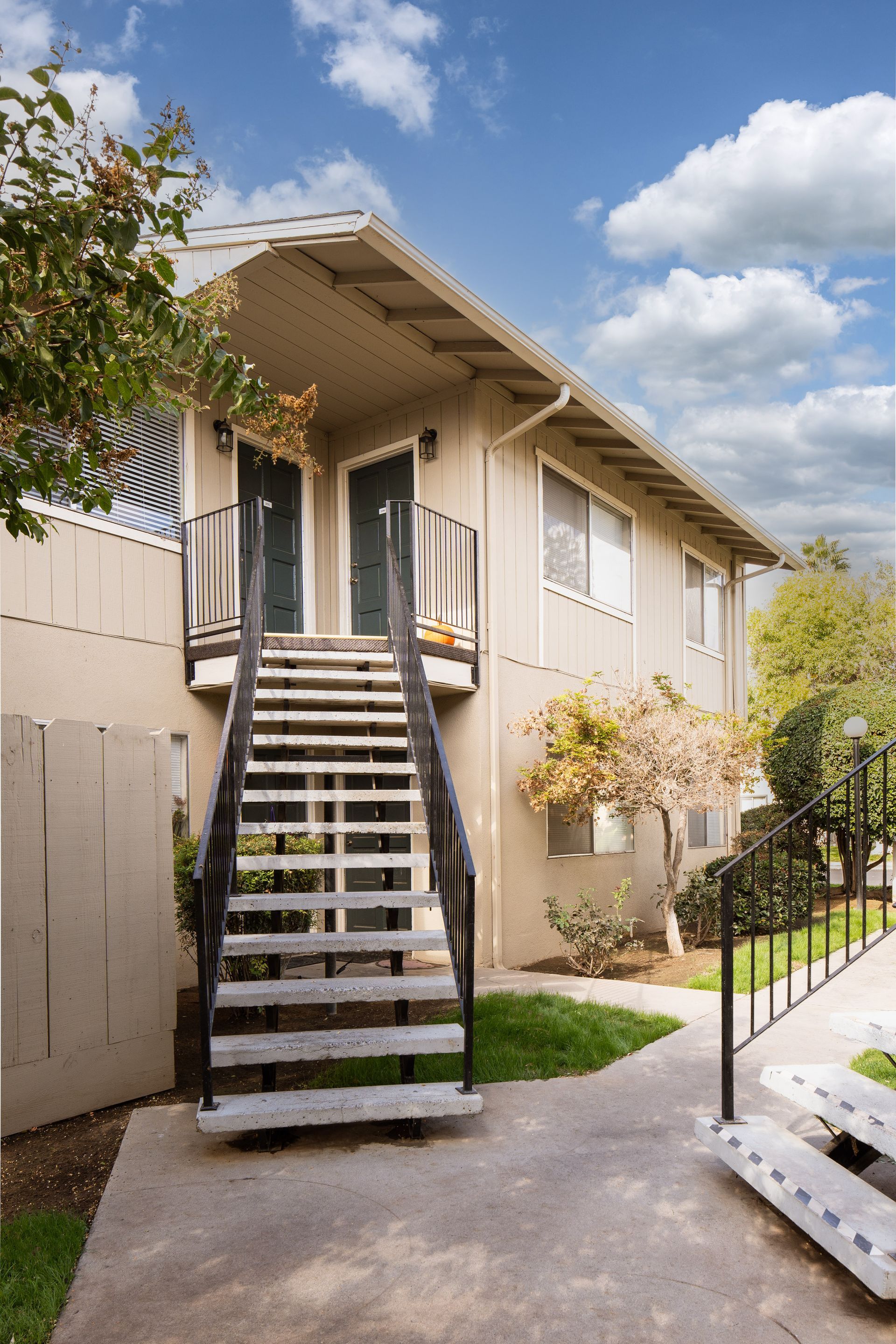 Exterior view of a two-story beige apartment building with outdoor stairs leading to two doors.