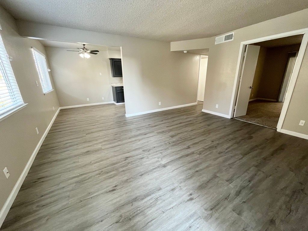 Empty living room with light gray wood-look flooring, neutral walls, and doorways leading to other rooms.