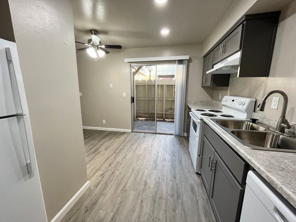 Kitchen interior with grey cabinets, white appliances, and a sliding door to a small patio.