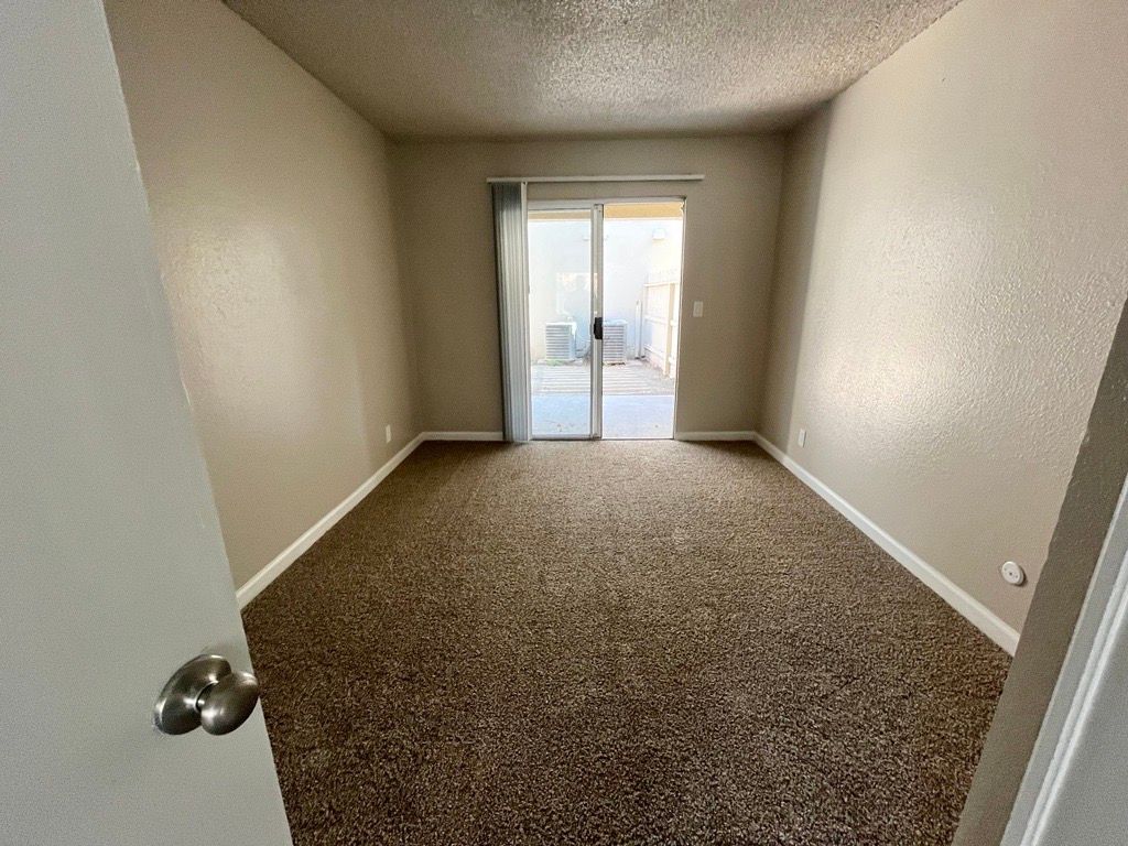 A carpeted room with a sliding glass door to a patio, tan walls.