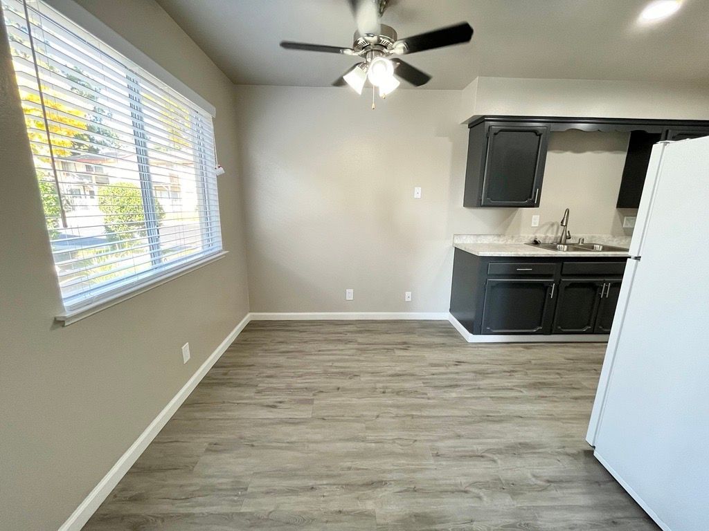 Kitchen area with grey walls, dark cabinets, window, and a ceiling fan.