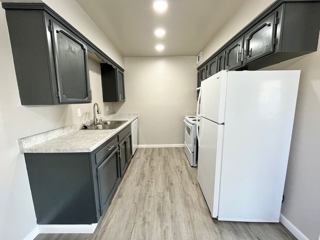 Narrow kitchen with gray cabinets, white appliances, and light wood-look flooring.
