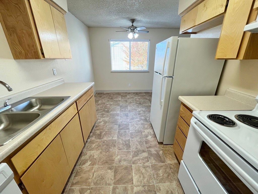 Kitchen with light wood cabinets, white appliances, and tan flooring.