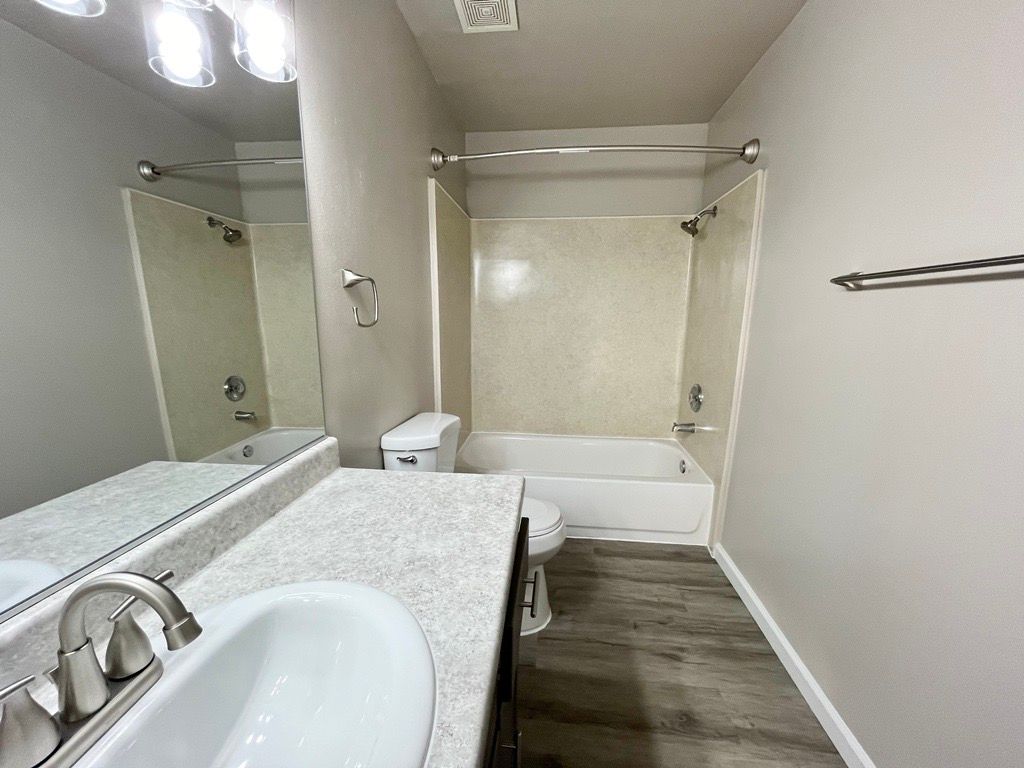 Bathroom with white sink, toilet, and tub. Grey walls, and wood-look floor.