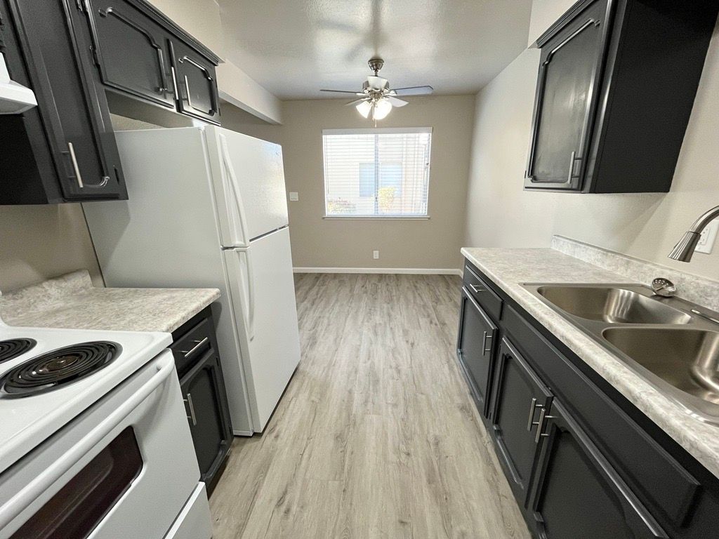 Kitchen with black cabinets, white appliances, and a view of the dining area.