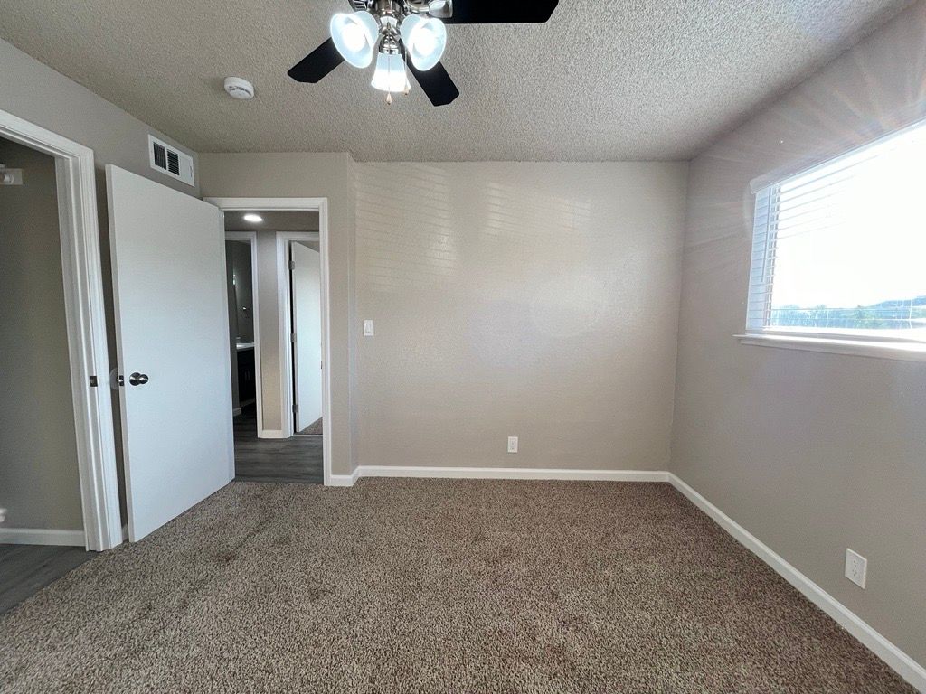 Empty bedroom with beige walls, brown carpet, white door, and ceiling fan.