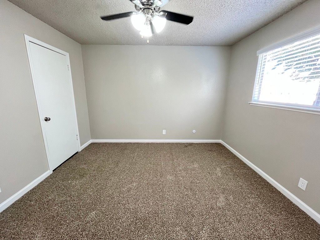 Empty bedroom with beige walls, brown carpet, white door, and a window.
