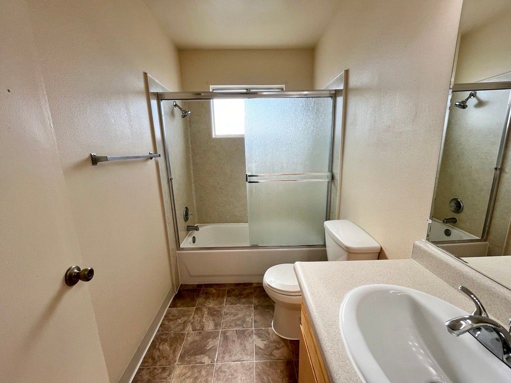 Bathroom with a bathtub/shower, toilet, sink, and brown tile flooring.