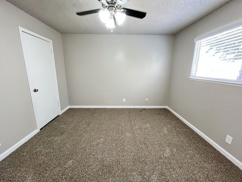 Empty room with tan carpet, beige walls, white door, and a window.