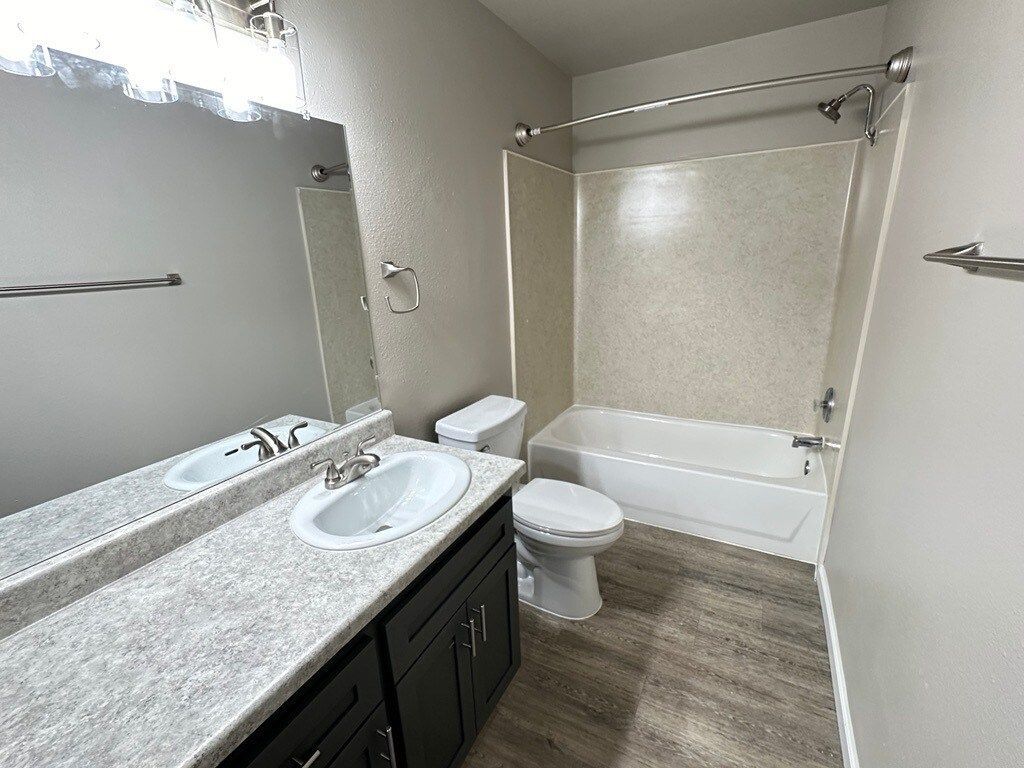 Bathroom with a sink, toilet, and bathtub/shower combo. Neutral colors with light brown flooring.