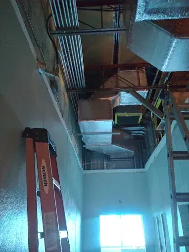 Interior ceiling construction view: HVAC ducts, electrical conduit, ladders, and freshly painted walls.