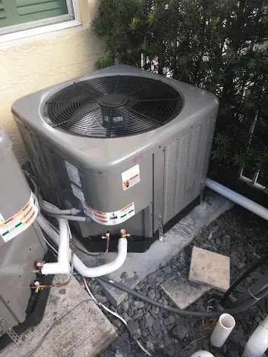 Gray air conditioning unit outside a building with white pipes.