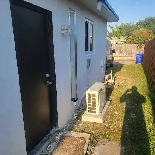 Black door and air conditioning unit on a white building exterior with a grassy side yard.