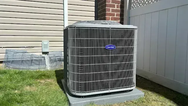 Air conditioner unit on a concrete pad, next to a beige house and white fence.