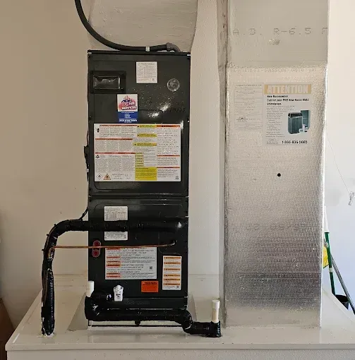 HVAC unit with ductwork and a black flexible pipe in a utility room.