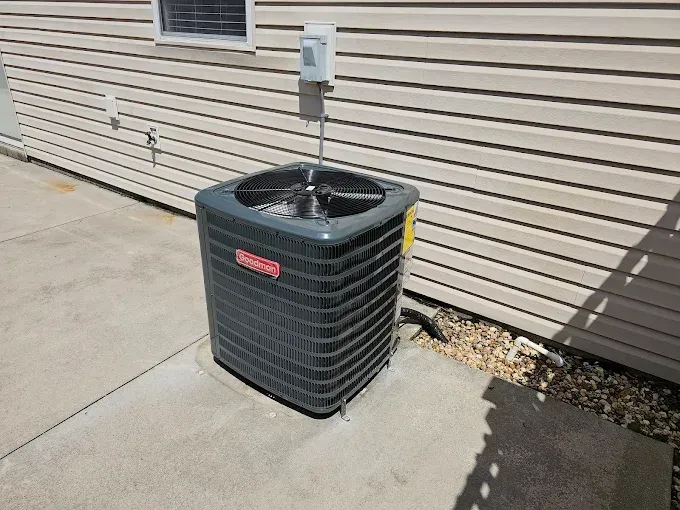 Outdoor air conditioning unit next to a beige house, on a concrete pad.