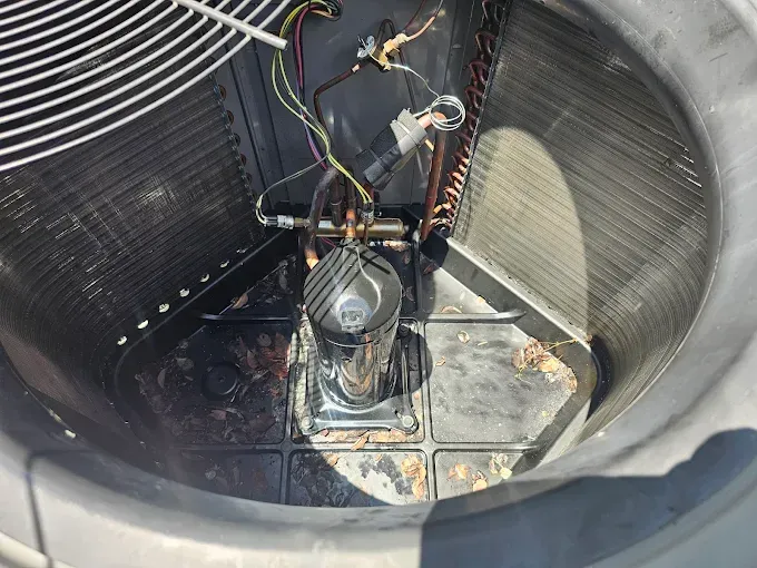 An air conditioner's interior. A compressor sits in the center with coils and fan blades surrounding it.