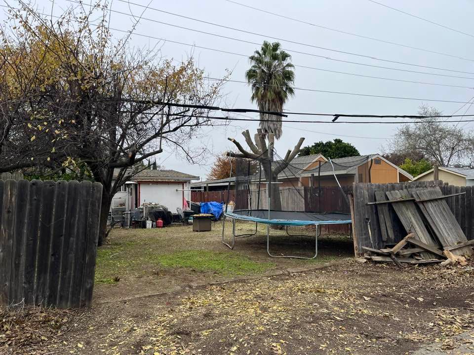 Backyard with trampoline, shed, fence, and tree under overcast sky.
