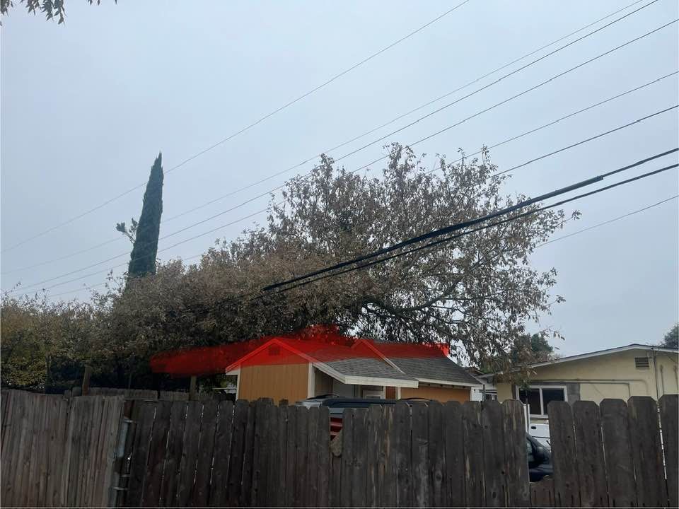 A house with a red roof behind a wooden fence, beneath power lines and a cloudy sky.