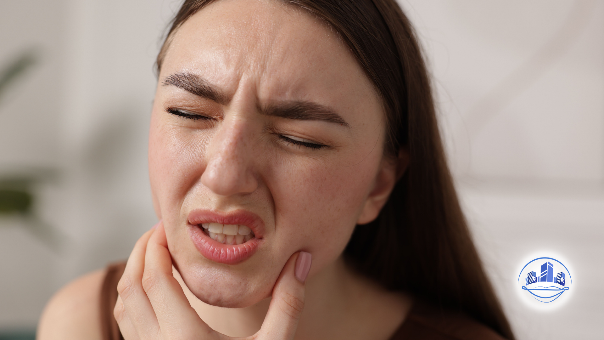 Woman holding face in pain, eyes closed, white tank top, light background.