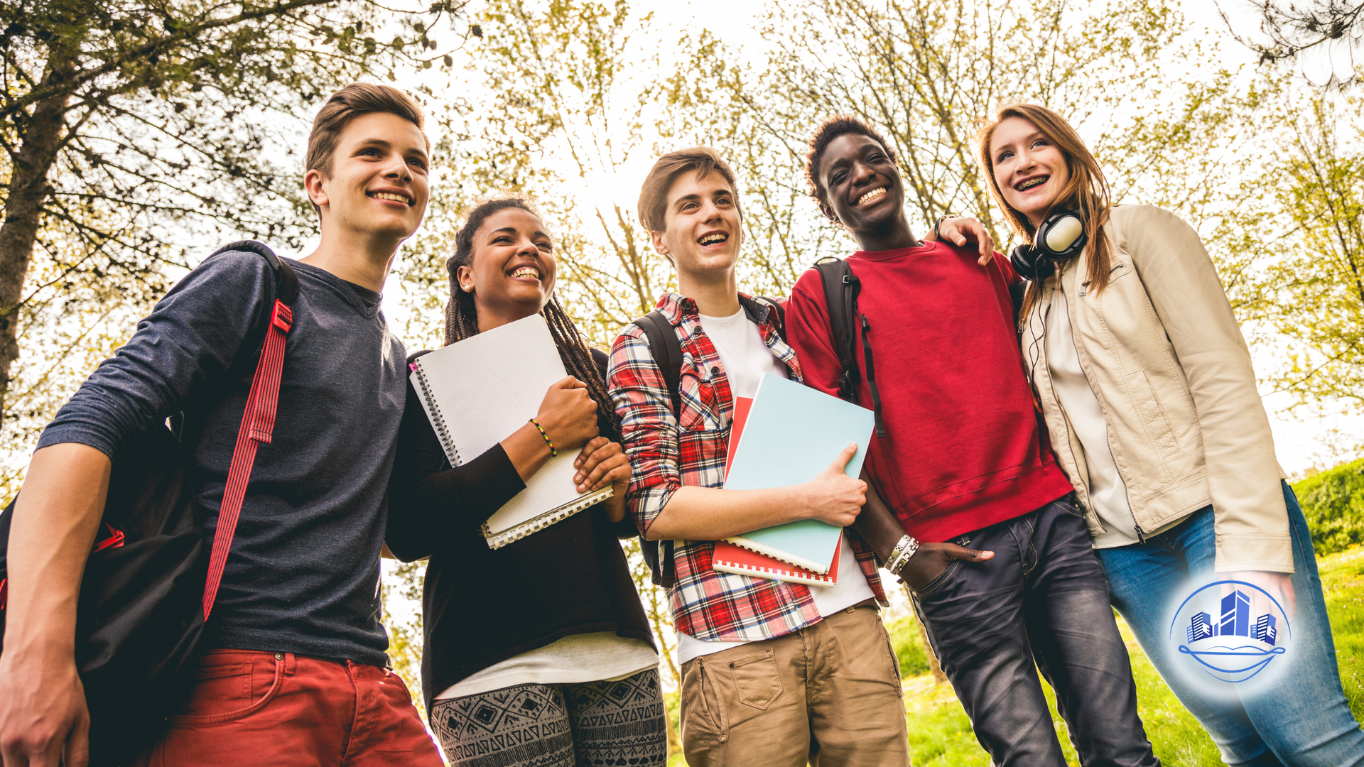 Four smiling people huddle together under a blue sky, arms around each other, looking down.