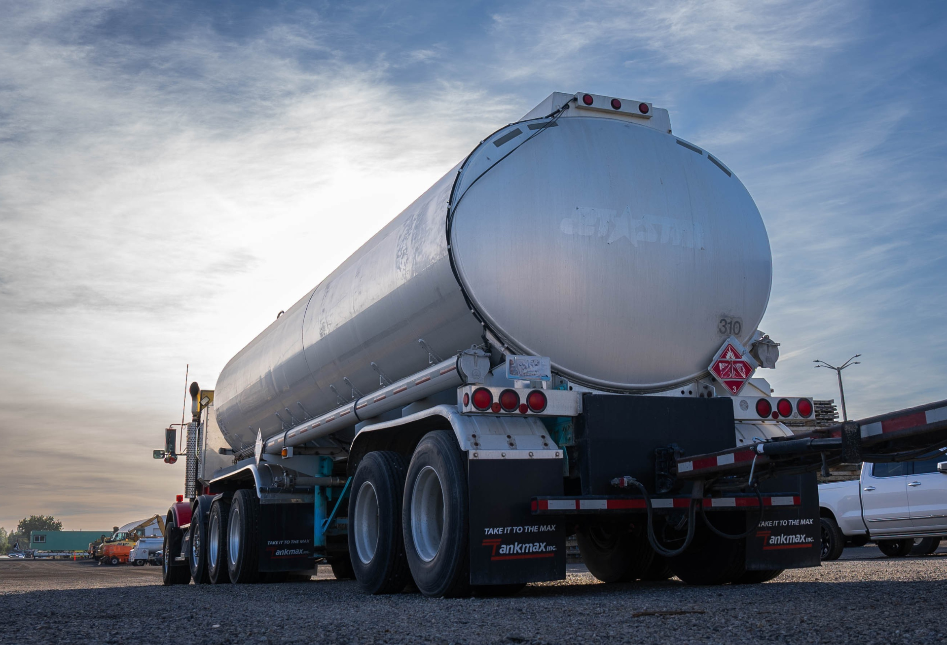 A large, silver tanker truck parked on a gravel lot under a cloudy sky.