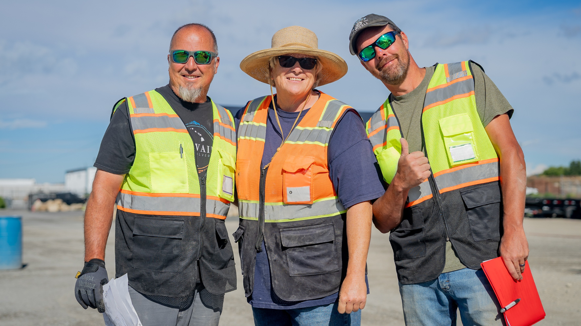Two CDL students smiling with a CDL instructor wearing safety vests in a CDL training yard.
