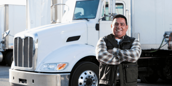 new truck driver student standing with arms crossed in front of a semi-truck smiling