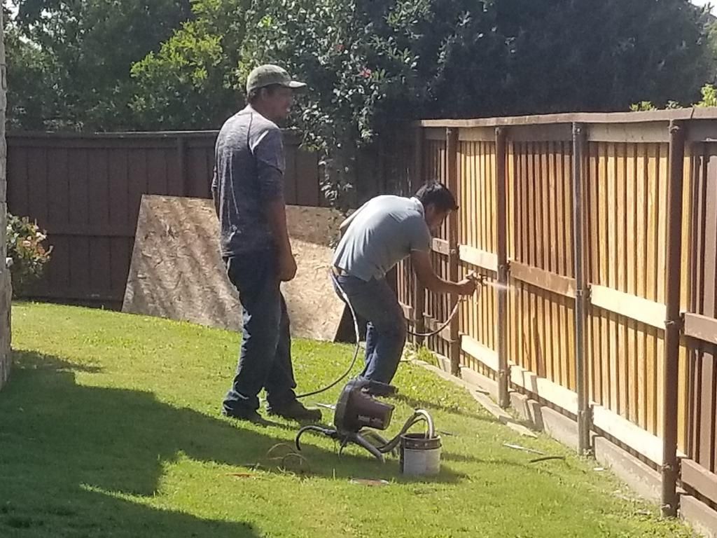 Two men are painting a wooden fence in a backyard