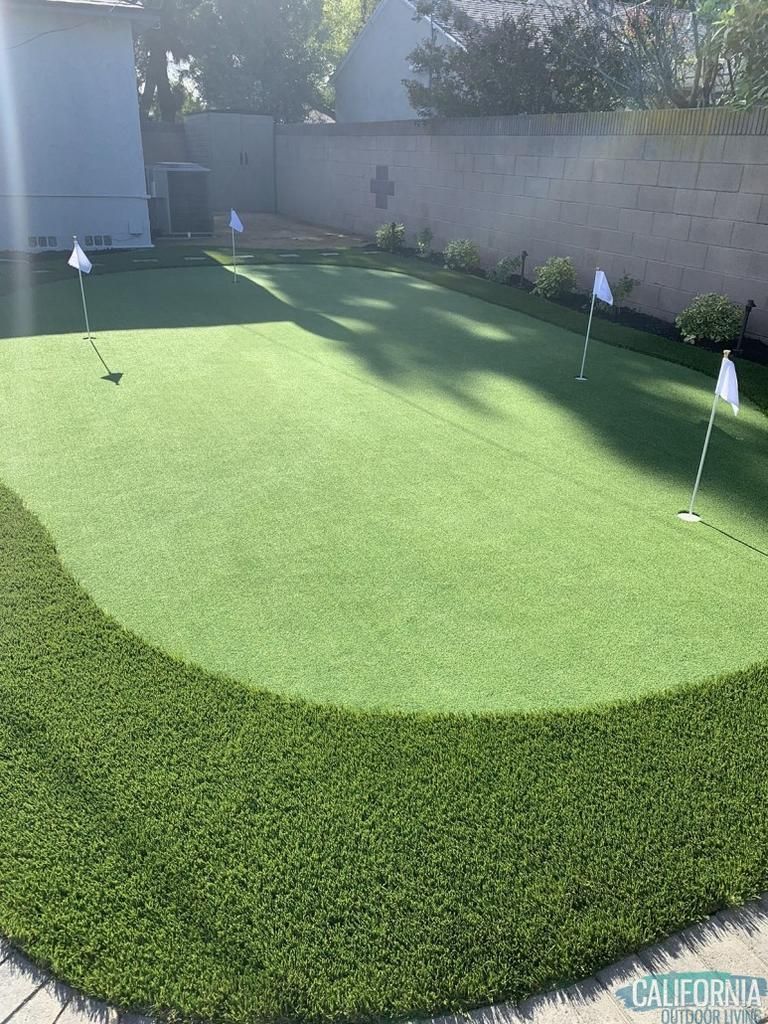 There is a putting green in the backyard of a house.