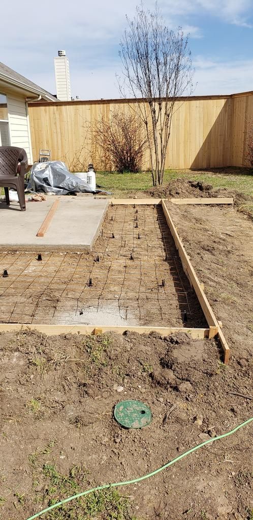 A concrete patio is being built in a backyard with a wooden fence.