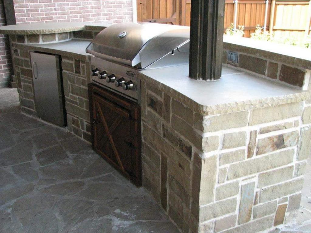 A grill is sitting on top of a stone counter next to a brick wall.