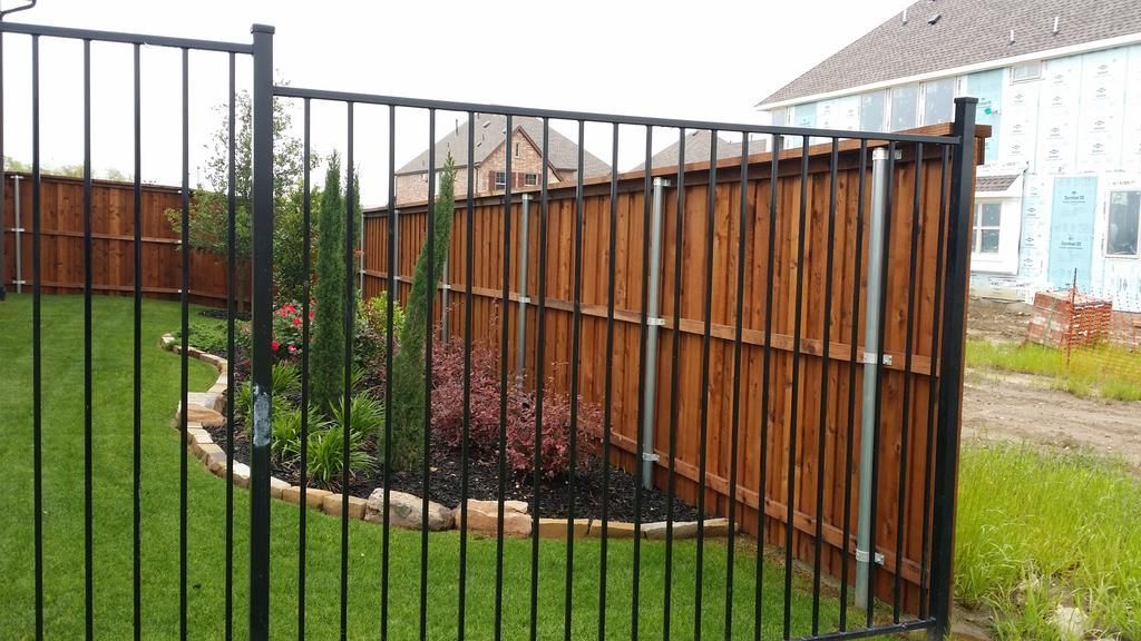A black metal fence surrounds a wooden fence in a backyard.