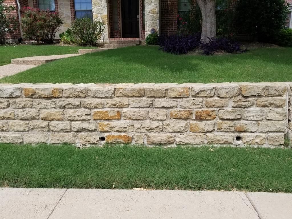 A brick wall in front of a house with a lush green lawn.