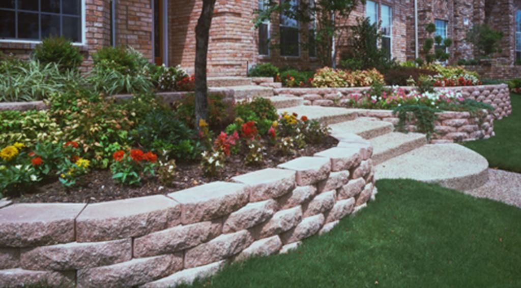 A stone wall surrounds a lush green lawn in front of a brick house.