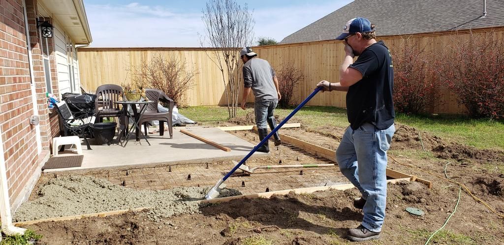 A man is raking dirt in a backyard in front of a house.