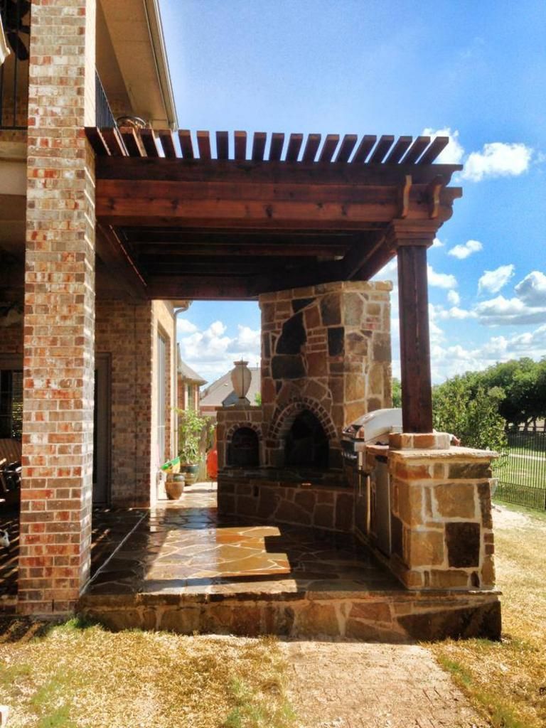 A brick house with a wooden pergola over a stone fireplace.