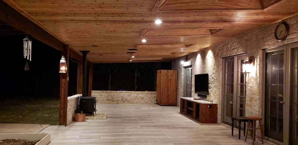 A large covered porch with a wooden ceiling and a television.