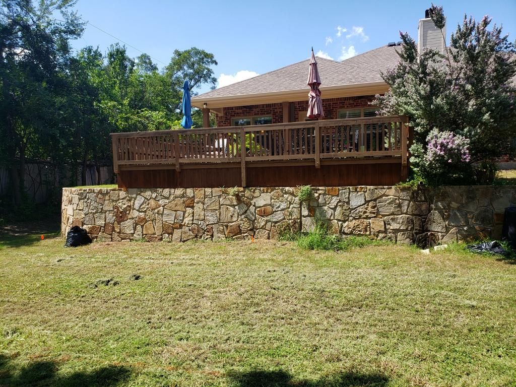 A large house with a large deck and a stone wall in the backyard.
