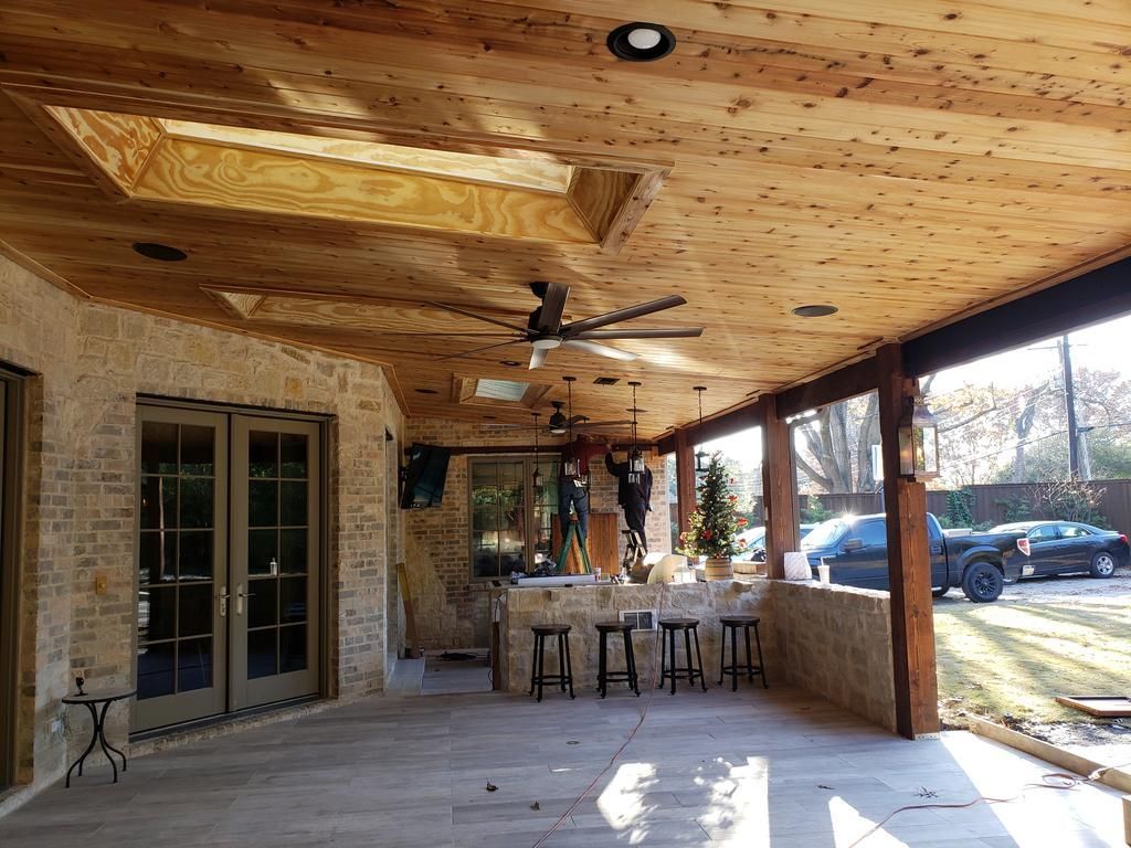 A large covered patio with a wooden ceiling and stools.