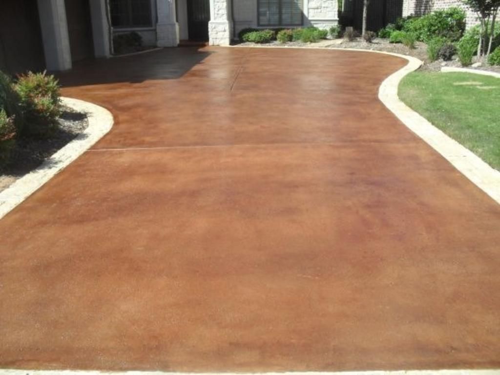 A brown concrete driveway leading to a house