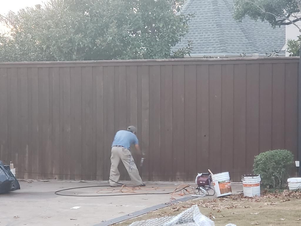 A man is painting a wooden fence in a driveway.
