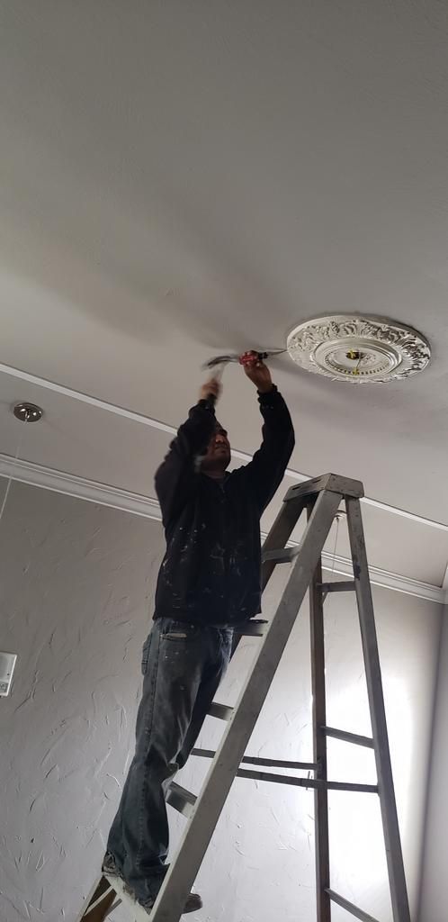 A man is standing on a ladder fixing a light fixture on the ceiling.