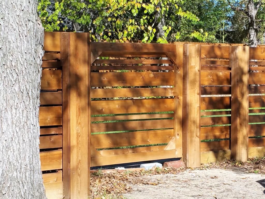 A wooden fence with a gate is surrounded by trees.