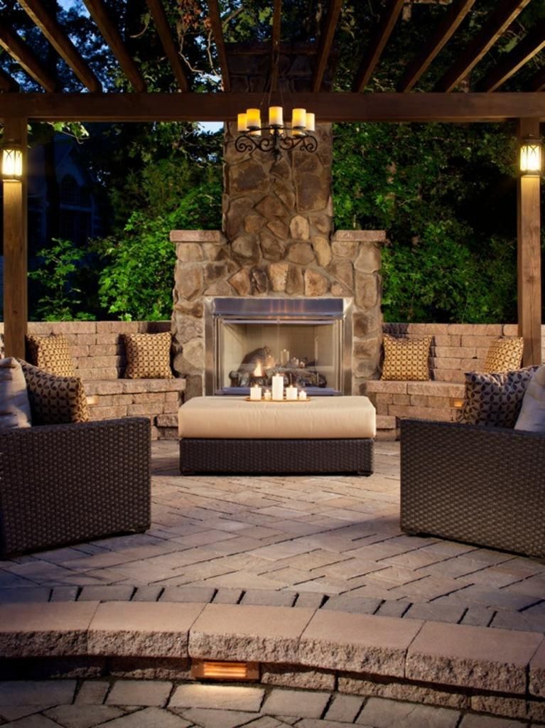 a patio with a fireplace and chairs under a pergola