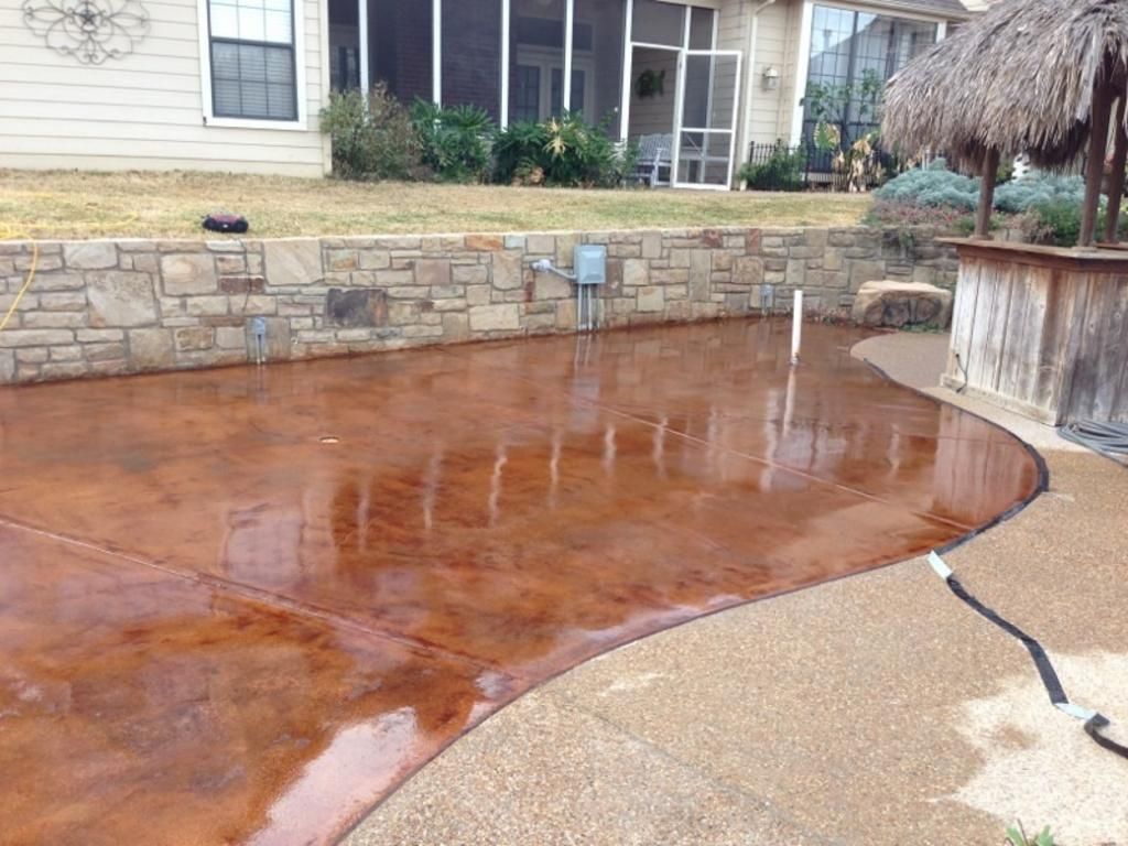 A concrete patio with a stone wall and a hose in front of a house.