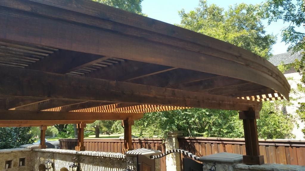 A wooden structure with a curved roof is surrounded by trees.