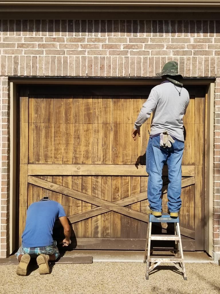 two men are working on a wooden garage door