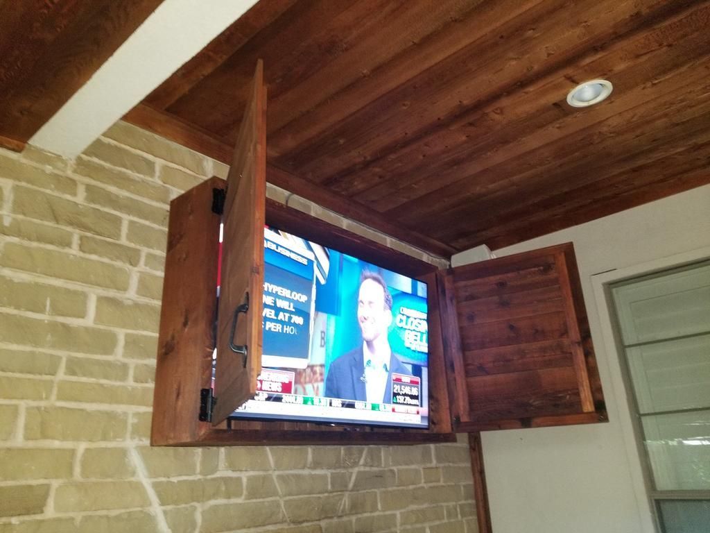 A television is mounted on a brick wall in a wooden cabinet