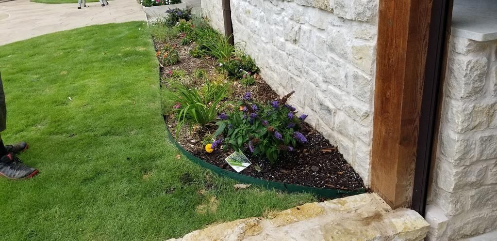 A person is standing next to a stone wall with a garden in front of it.